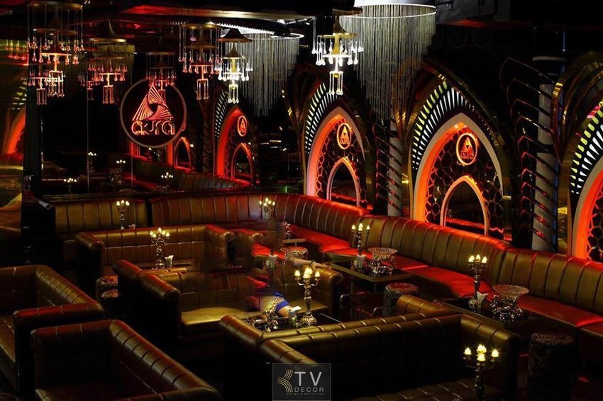 Không gian quán cafe bar thiết kế theo phong cách sang trọng, sử dụng sofa da, ánh sáng đỏ – nâu ấm, kết hợp đèn chùm và trang trí tường họa tiết hoàng gia tạo cảm giác đẳng cấp và ấm cúng.