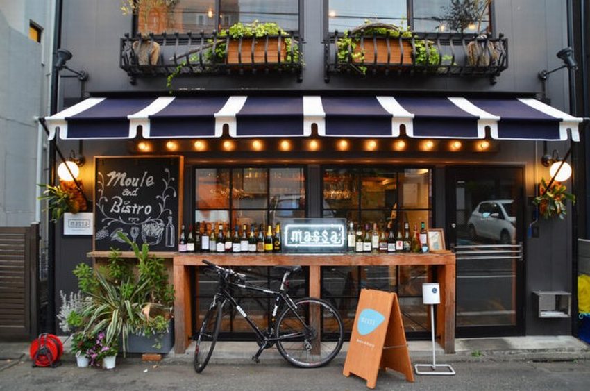 Thiết kế quán cafe phong cách châu Âu hiện đại với mặt tiền nổi bật, mái hiên sọc xanh – trắng, trang trí cây xanh và không gian gần gũi, thu hút.