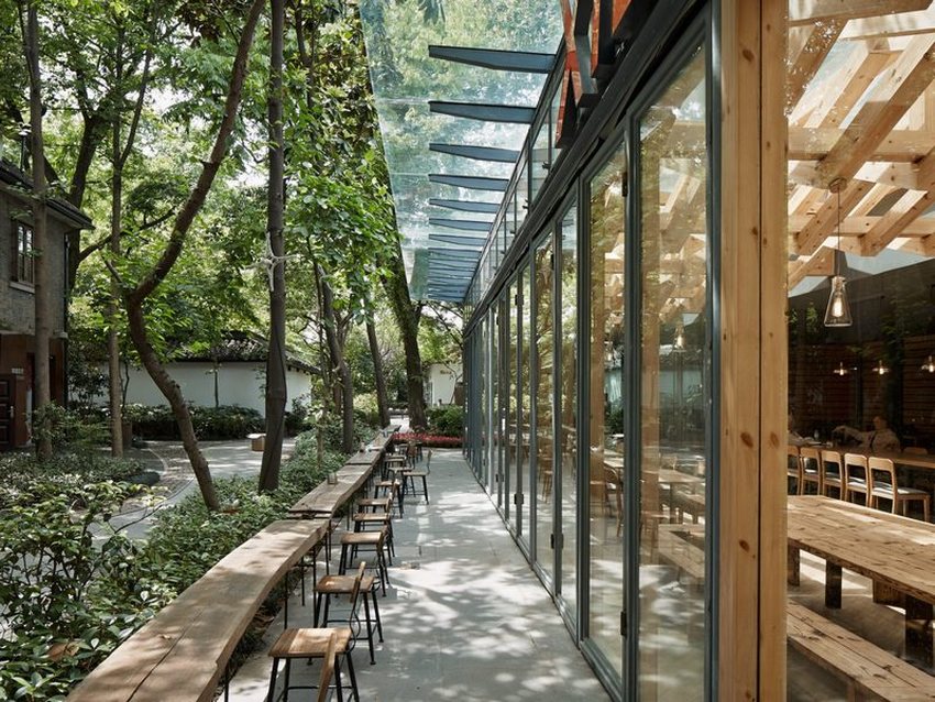 Thiết kế thi công quán cafe khung thép hiện đại với không gian mở, tường kính lớn nhìn ra khu vườn xanh mát, tạo trải nghiệm gần gũi thiên nhiên.