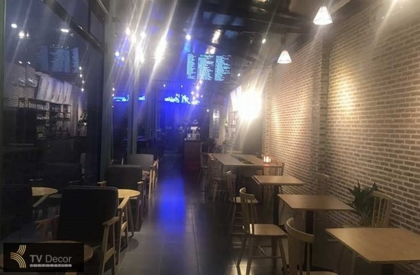 Thiết kế quán cafe khung thép hiện đại với không gian sâu, trần cao thoáng đãng, tường gạch thô, ánh sáng trang trí nổi bật và nội thất gỗ tối giản mang phong cách công nghiệp hiện đại.