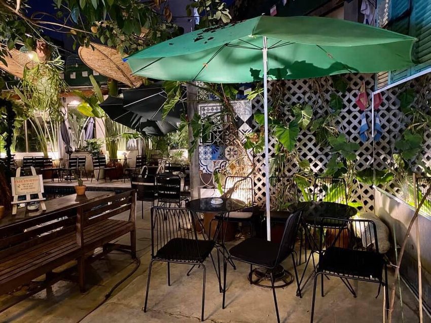 Quán cafe sân vườn buổi tối với ánh sáng lung linh, bàn ghế ngoài trời và ô che tạo không gian thoải mái, gần gũi với thiên nhiên.