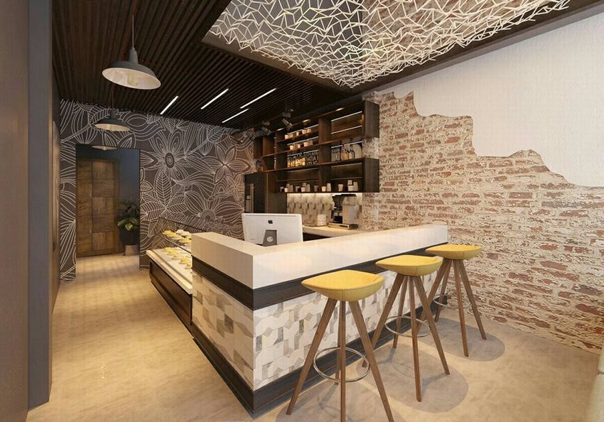 Không gian quán cafe trà sữa với quầy bar hiện đại, ghế cao màu vàng, tường gạch thô kết hợp họa tiết hoa lớn và trần nhà trang trí lưới ánh sáng nghệ thuật.