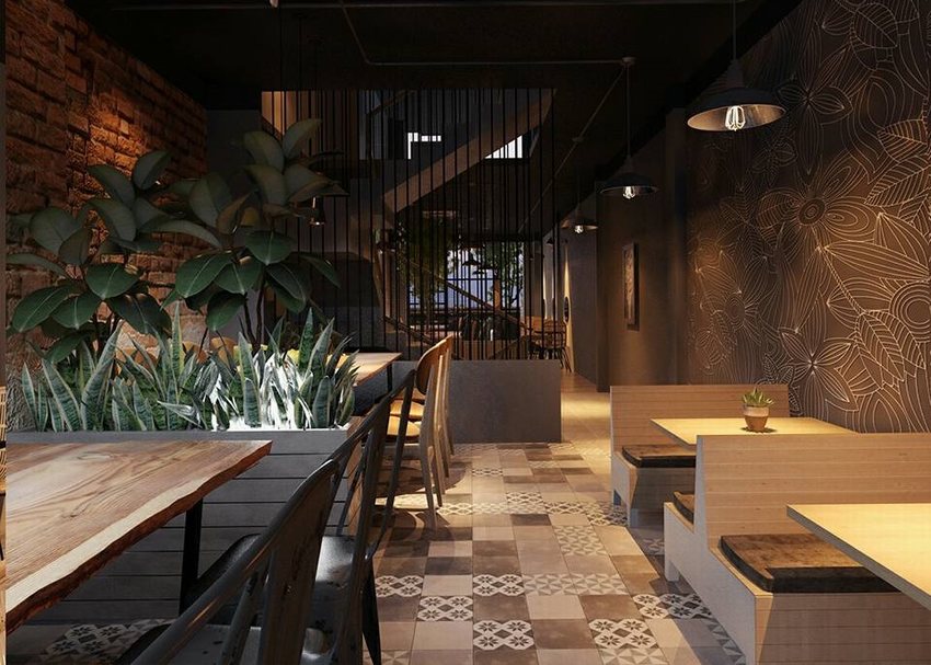 Không gian quán cafe trà sữa với tường gạch đỏ, vách ngăn sắt, sàn gạch bông, đèn thả trần ánh sáng vàng, cây xanh trang trí và bàn ghế gỗ tối màu, mang phong cách tối giản hiện đại.