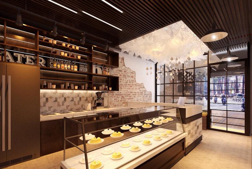 Không gian nội thất quán cafe trà sữa hiện đại với quầy trưng bày bánh ngọt, tường gạch thô, trần đèn nghệ thuật và cửa kính lớn hướng ra phố.