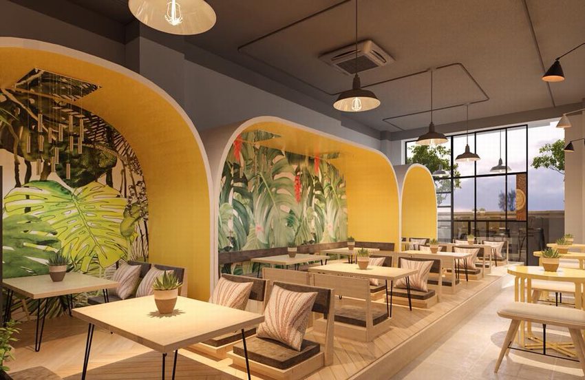 Quán cafe trà sữa thiết kế theo phong cách nhiệt đới với vòm vàng nổi bật, tranh lá cây lớn trên tường, bàn ghế gỗ, cửa kính lớn đón ánh sáng và cây xanh tạo điểm nhấn.