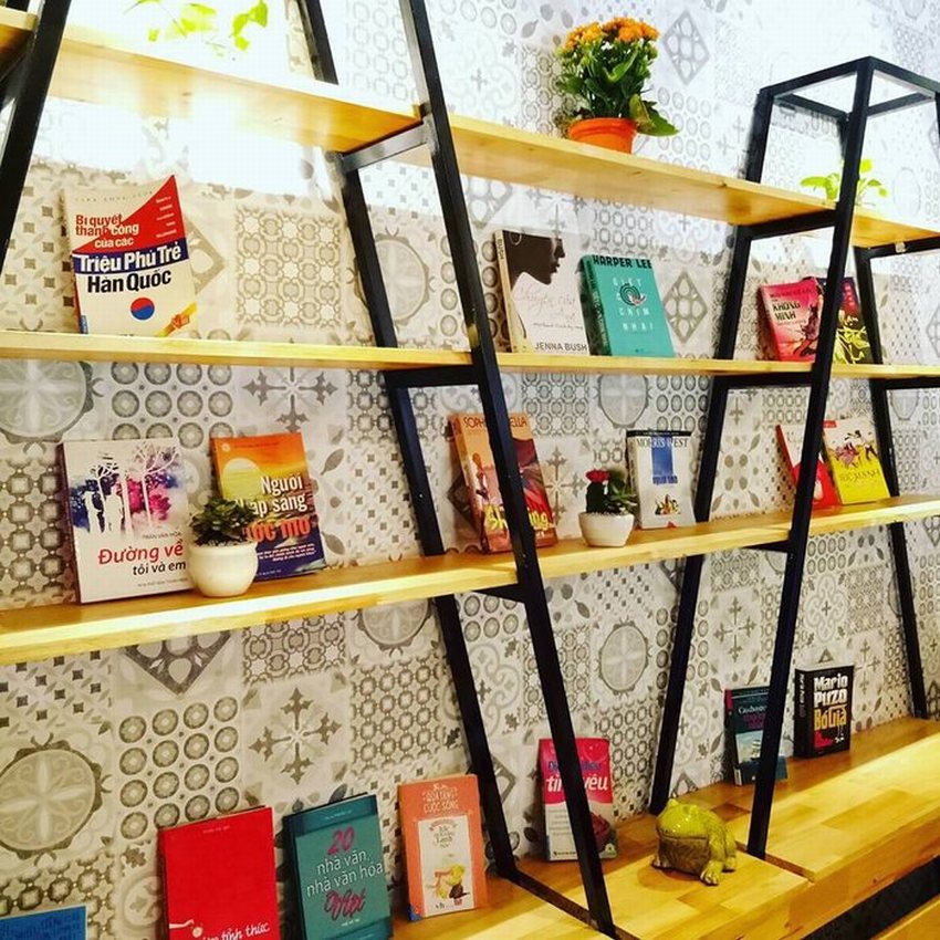 Kệ sách gỗ khung sắt trong quán cafe trà sữa, trang trí nhiều đầu sách hay cùng chậu cây xanh nhỏ, tạo không gian thư giãn cho khách.