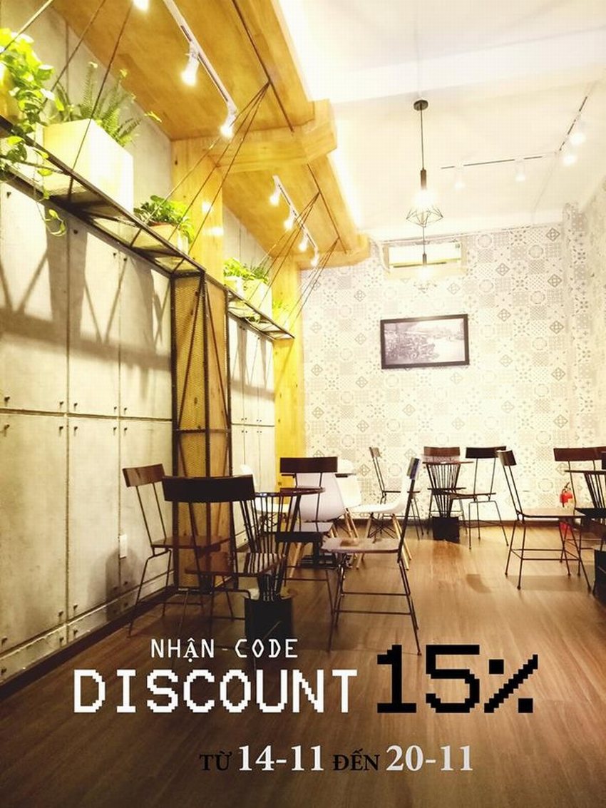 Không gian quán cafe trà sữa với bàn ghế gỗ tối giản, kệ treo cây xanh trên tường và ánh đèn vàng ấm áp, mang đến cảm giác gần gũi, thư giãn.
