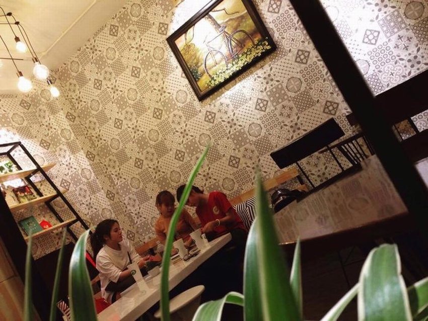 Thiết kế nội thất quán cafe trà sữa đẹp, bàn ghế gỗ tối giản, kệ treo cây xanh trang trí và ánh sáng vàng ấm cúng, tạo không gian thoải mái cho khách hàng.