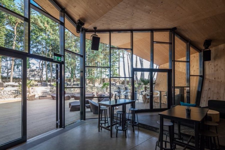 Nội thất nhà hàng kiến trúc góc cạnh hiện đại, trần gỗ ấm áp, quầy bar tinh tế, ánh sáng đèn thả nghệ thuật, không gian mở thoáng đãng. 