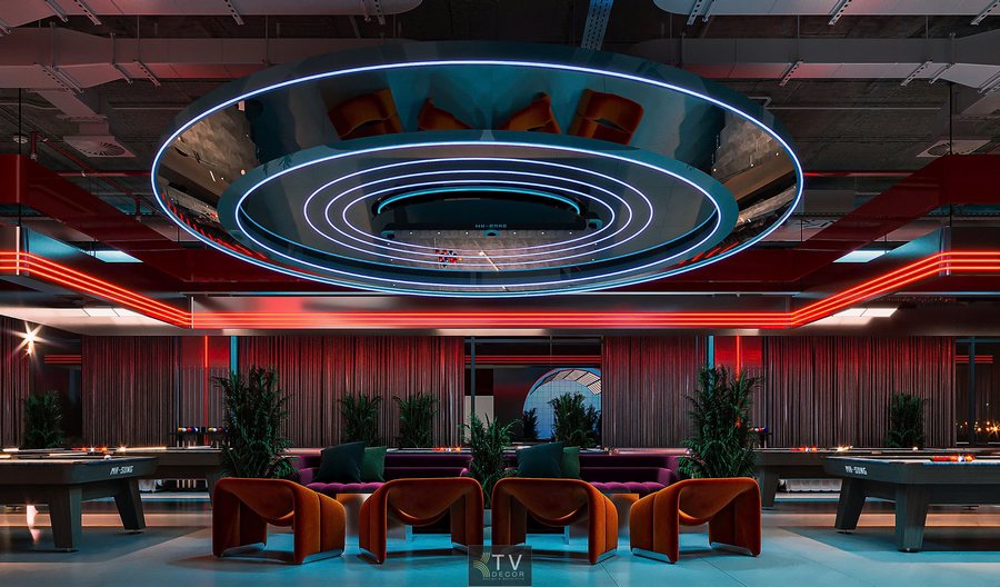 Góc nhìn dọc trục chính khu bida, nhấn mạnh chiều dài không gian. Trần kỹ thuật mở, đèn LED treo song song. Bàn bida tiêu chuẩn, ghế sofa chờ hai bên, sàn phẳng dễ di chuyển, âm thanh phân bổ đều.