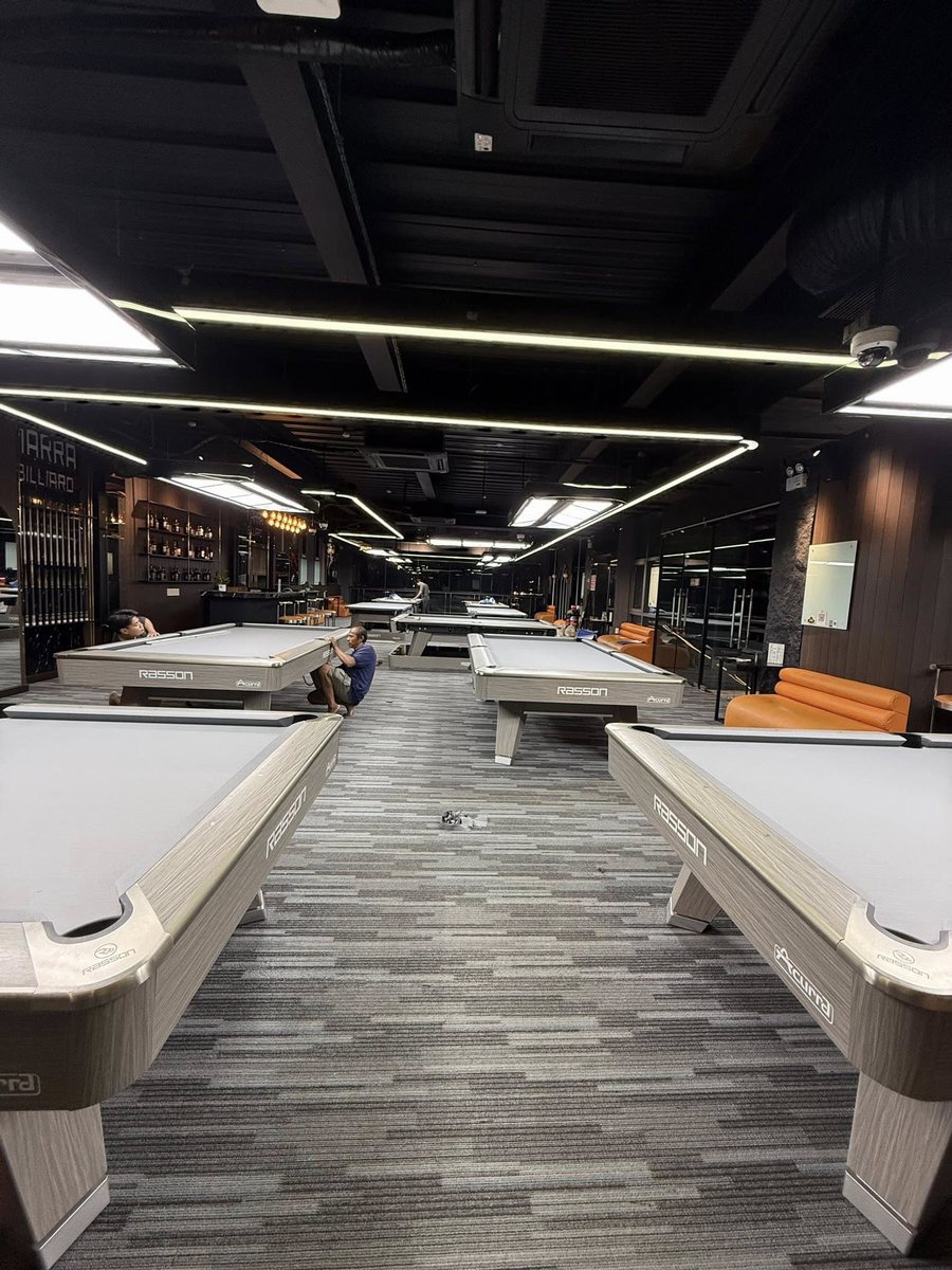 Không gian bida NARRA BILLIARDS được bố trí gọn gàng với dãy bàn thi đấu tiêu chuẩn, trần đen kết hợp đèn LED tuyến tính tạo cảm giác hiện đại và chiều sâu. Sàn trải thảm xám, sofa da cam nổi bật, mang lại trải nghiệm chơi bida chuyên nghiệp – thoải mái – cao cấp. 