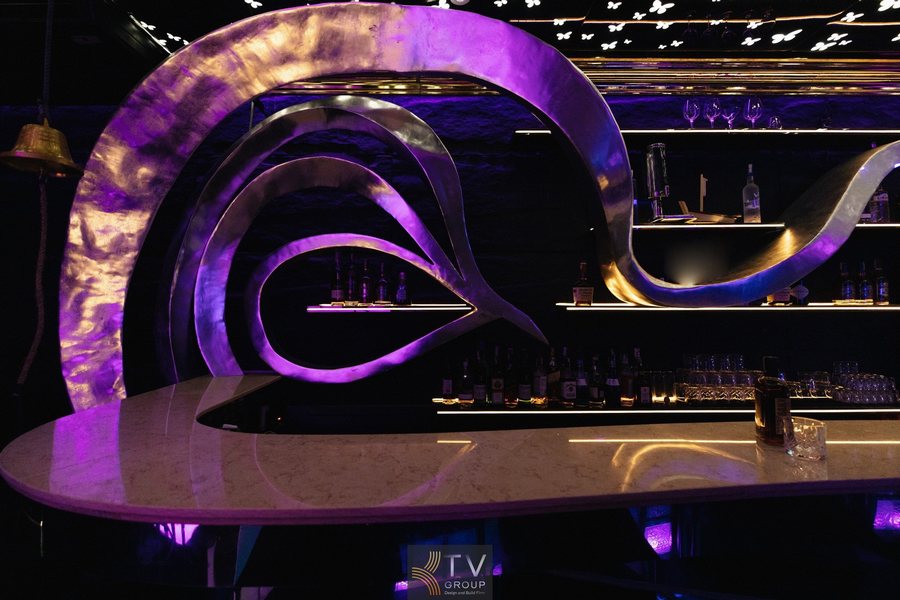 Góc quầy bar lounge mini 100m² tại Huỳnh Thúc Kháng được thiết kế cong mềm mại, kết hợp trần sao LED và ánh sáng tím xanh, tạo điểm nhấn mạnh cho không gian giải trí đêm. 