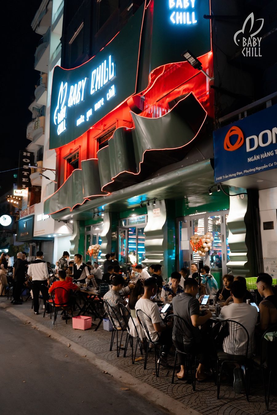 Mặt tiền nhà hàng lounge bar với bảng hiệu ánh sáng nổi bật, thu hút đông khách ngồi ngoài trời, tạo không khí kinh doanh sôi động.